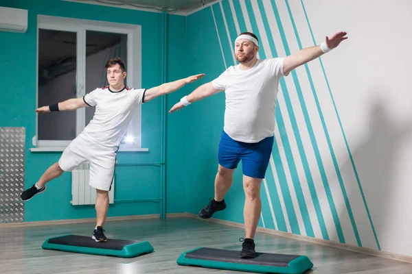 O homem gordo é muito trabalhador fazendo exercícios em passos com as mãos para cima durante as aulas de fitness em grupo. Peso em excesso — Fotografia de Stock