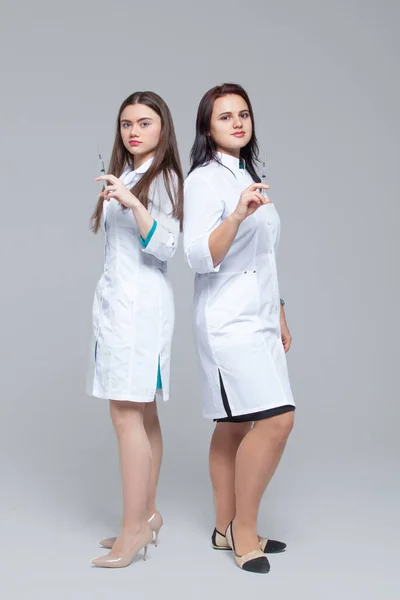 Полноразмерный портрет двух женщин-врачей, стоящих спиной к спине и готовых к введению шприцов — стоковое фото
