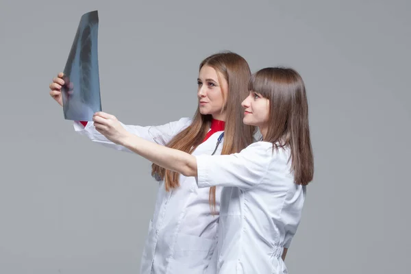 Két fiatal női orvos nézte az x-ray képet a tüdő szürke háttér — Stock Fotó
