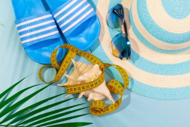 Çizgili şapka, güneş gözlüğü, deniz kabuğuyla ölçüm bandı ve turkuaz mavi arka planda bir palmiye dalı. Denizde bir tatil için kilo verme kavramı. Reklam alanı