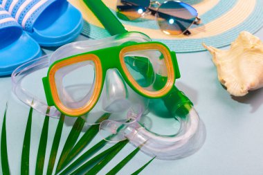 Turkuaz mavi arka planda plaj aksesuarları - güneş gözlükleri, mavi terlikler, çizgili şapka, dalış maskesi, kabuk ve palmiye yaprağı. Plaj tatili kavramı, deniz turu, sıcak güneşli yaz.