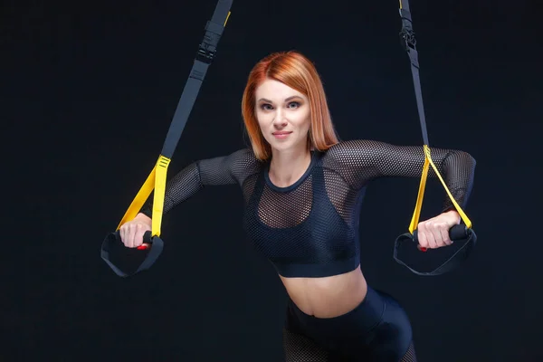 Belo treinamento de mulher fitness com tiras de fitness trx em sportswear sexy isolado no fundo preto — Fotografia de Stock