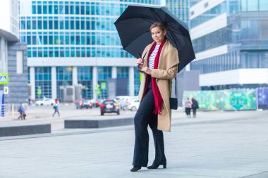 Yağmur. Açık havada yaşayan esmer bir kızın moda portresi. Şehir caddesinde yürüyorum. Alışverişe. Şık, beyaz montlu, kırmızı yakalı, siyah şemsiyeli bir baston giyiyor. İş kadını.