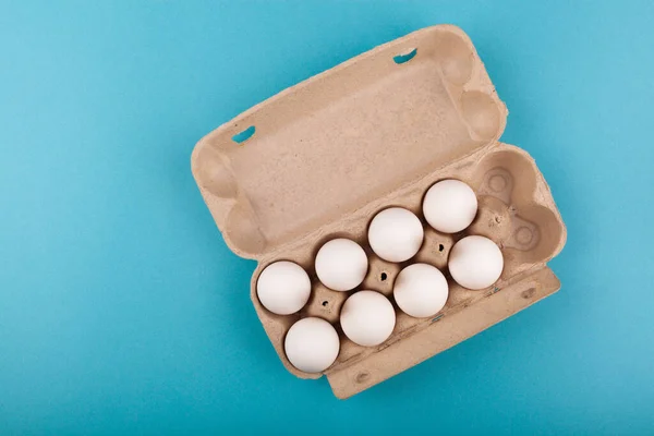 Huevos de pollo. Vista superior de una caja gris abierta con huevos blancos. Aislado sobre un fondo azul. El concepto de un estilo de vida saludable, obtener proteínas puras. Desayuno apropiado. Ocho huevos. . — Foto de Stock