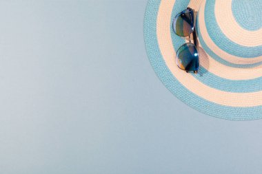 Turkuaz mavi arka planda plaj aksesuarları - güneş gözlüğü ve çizgili mavi şapka. Plaj tatili kavramı, deniz turu, sıcak güneşli yaz. Reklam alanı