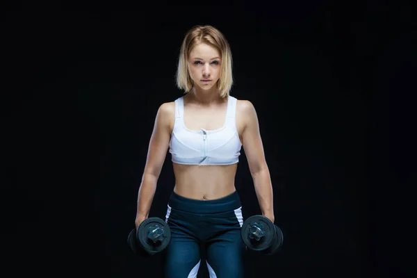 Retrato de cerca de una chica joven musculosa posando con pesas en el gimnasio aislado sobre un fondo negro —  Fotos de Stock