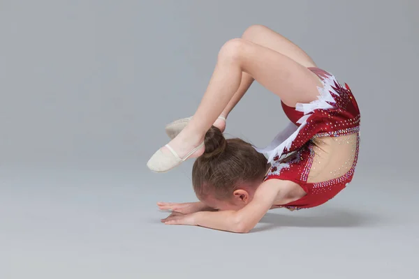 Menina flexível em belo vestido vermelho está fazendo exercícios de ginástica no chão em fundo cinza — Fotografia de Stock