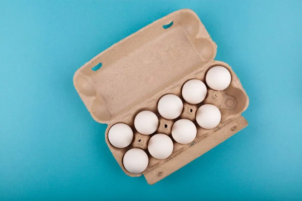 Huevos de pollo. Vista superior de una caja gris abierta con huevos blancos. Aislado sobre un fondo azul. El concepto de un estilo de vida saludable, obtener proteínas puras. Desayuno apropiado. Nueve huevos . — Foto de Stock