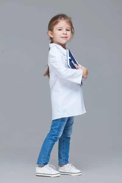 Roztomilé dítě dívka uniformované jako lékař drží lékařské záznamy izolované na šedém pozadí — Stock fotografie