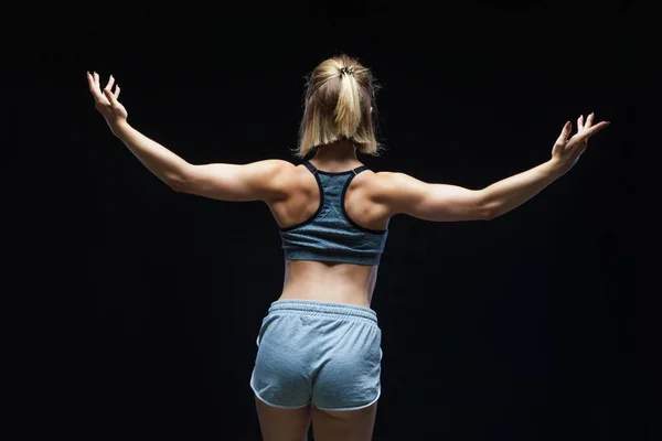 Vista posterior de la fuerte chica deportiva en la parte superior y pantalones cortos de jean que muestran los músculos en el fondo negro —  Fotos de Stock