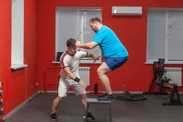 Ansioso homem com excesso de peso está fazendo saltar no ginásio sob a orientação de um personal trainer — Fotografia de Stock