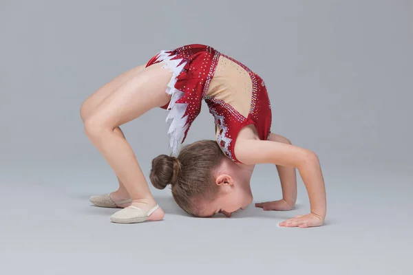Menina flexível em belo vestido vermelho está fazendo exercícios de ginástica no chão em fundo cinza — Fotografia de Stock