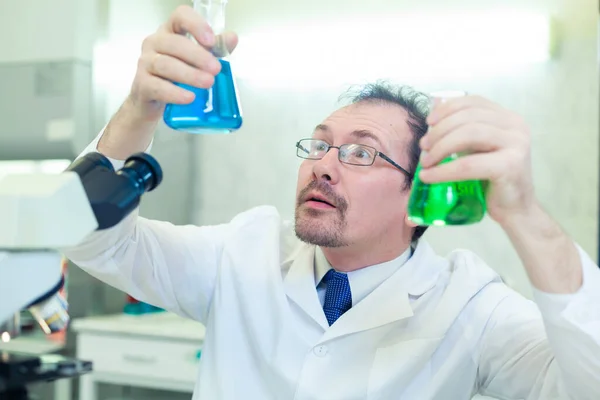 Chemist crazy. A mad scientist conducts experiments in a scientific laboratory. With surprised eyes, he examines the liquid in the flask through. COVID-19. COVID Coronavirus