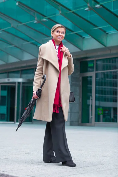 Buiten lifestyle modeportret van een prachtig brunette meisje. Wandelen op straat. Winkelen. Draag stijlvolle witte jas, rode neksjaal, zwarte paraplustok. Zakelijke vrouw. — Stockfoto