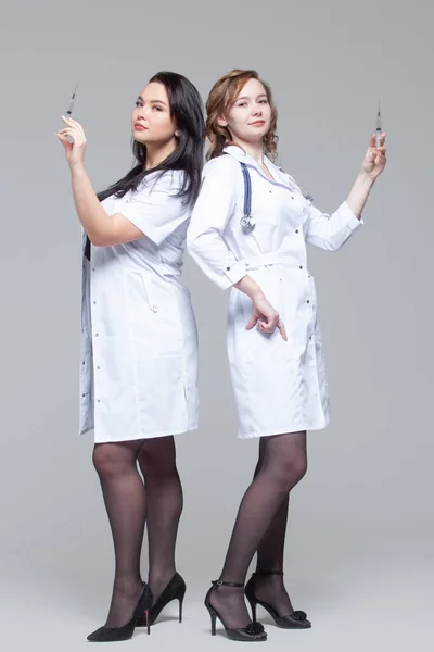 Pełna długość Portret dwóch kobiet lekarzy stojących back-to-back trzymać strzykawki gotowe do wstrzyknięcia — Zdjęcie stockowe