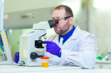 Laboratuvar çalışanı bir tıp laboratuarında mikroskop ve laboratuvar ekipmanları kullanarak idrar tahlili yapıyor.