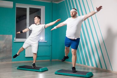 Şişman adam, grup fitness derslerinde elleri yukarıda merdivenlerde egzersiz yaparken çok çalışkandır. Fazla ağırlık