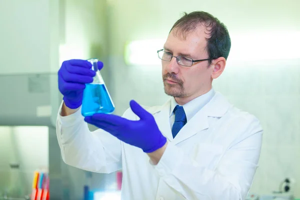 Вчений тримає і вивчає колбу з блакитною рідиною в науковій лабораторії. COVID-19. Коронавірус COVID — стокове фото