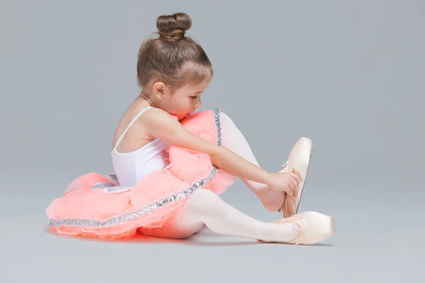 Симпатична чарівна балерина маленька дівчинка в рожевому туалеті сидить на підлозі, намагаючись одягнути балетне взуття — стокове фото