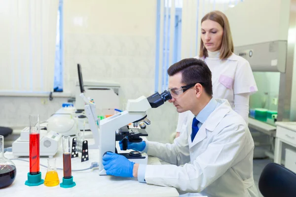 Επιστήμονας διεξάγει επιστημονική έρευνα κοιτάζοντας μέσα από μικροσκόπιο σε ένα ιατρικό εργαστήριο. Επιστήμονας με βοηθό. Κόβιντ-19. Ιός Covid Coronavirus — Φωτογραφία Αρχείου