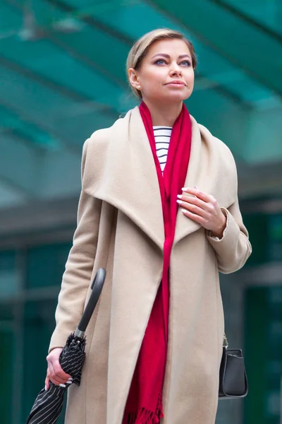 Buiten lifestyle modeportret van een prachtig brunette meisje. Wandelen op straat. Winkelen. Draag stijlvolle witte jas, rode neksjaal, zwarte paraplustok. Zakelijke vrouw. — Stockfoto