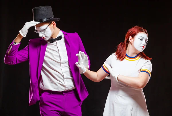 Portrait of two mime artists, isolated on black background. Young woman and man are drifting apart putting their hands forward. Symbol of separation, parting, quarrel