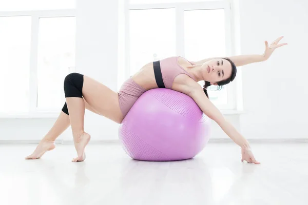 Menina esbelta jovem fortalece os músculos das costas com a ajuda de bola de fitness — Fotografia de Stock