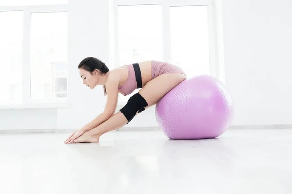 Slank sportief meisje doet stretching oefening reiken naar haar tenen zitten op fitness bal — Stockfoto