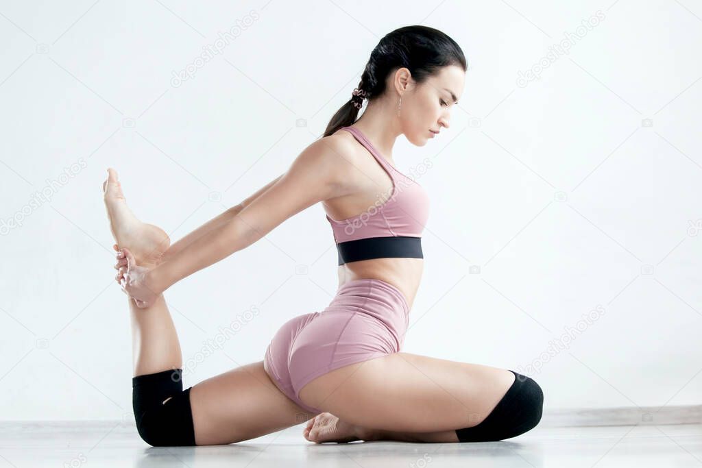 Young sporty woman in modern pink sportswear is sitting on the floor with bent leg doing stretching exercise