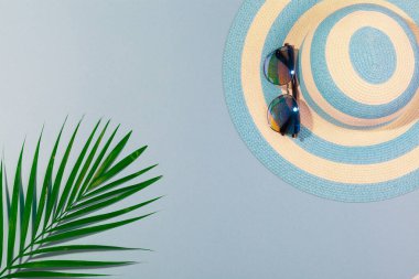 Turkuaz mavi arka planda plaj aksesuarları, güneş gözlüğü, mavi çizgili şapka ve palmiye yaprağı. Plaj tatili kavramı, deniz turu, sıcak güneşli yaz. Reklam alanı