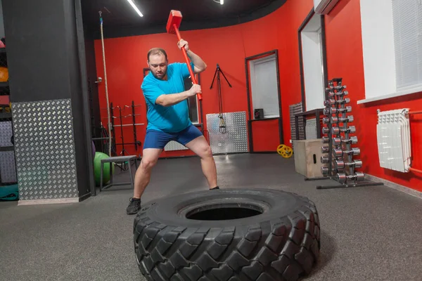 胖男人是一个非常坚持不懈的训练与大锤和轮胎在健身房。体重超标 — 图库照片