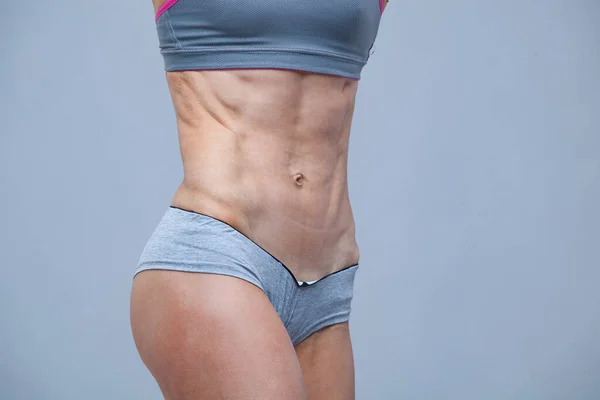 Primer plano de los músculos abdominales de la joven atleta sobre fondo gris —  Fotos de Stock
