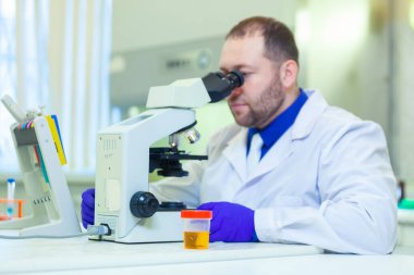 Laboratuvar çalışanı bir tıp laboratuarında mikroskop ve laboratuvar ekipmanları kullanarak idrar tahlili yapıyor.