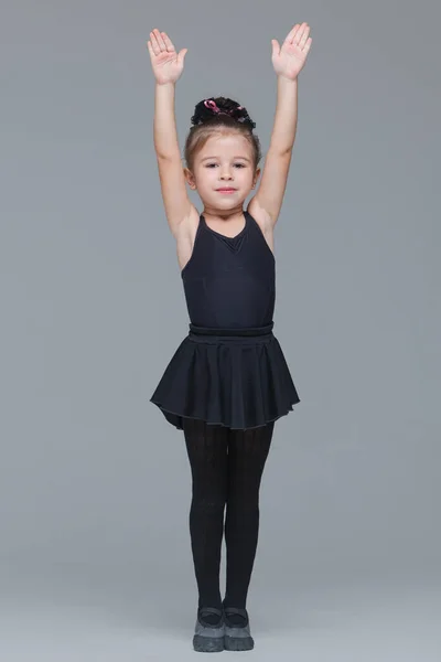 Bela menina ginasta em sportswear preto vai se tornar dançarina de balé e mostra exercícios em fundo cinza — Fotografia de Stock