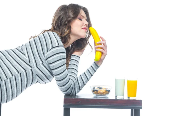 Uma jovem grávida senta-se a uma mesa em que se encontra uma banana, há uma placa com cereais, um copo com kefir e suco. O conceito de nutrição durante a gravidez. Isolado sobre um fundo branco . — Fotografia de Stock