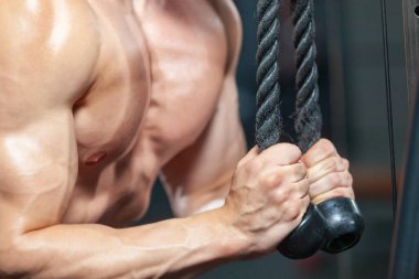 Modern spor salonunda trisepslerini spor malzemeleriyle çalıştıran güçlü kaslı adama yaklaş.