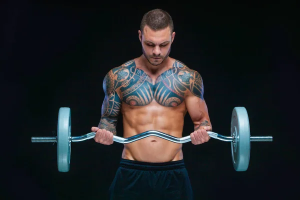 Getatoeëerde sterke gespierde atletische man pompen spieren met lange halter op zwarte achtergrond — Stockfoto