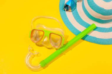 Sarı arka planda plaj aksesuarları, çizgili mavi şapka ve dalış maskesi. Plaj tatili kavramı, deniz turu, sıcak güneşli yaz. Reklam alanı