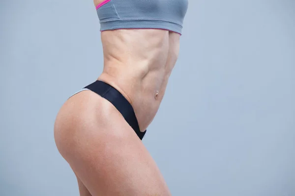Крупним планом м'язи живота молодої дівчини спортсменки на сірому фоні — стокове фото
