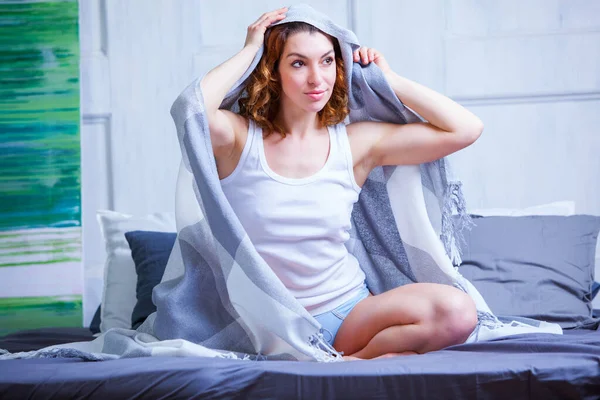 Menina bonita em um top branco coberto com uma xadrez azul sentado na cama — Fotografia de Stock