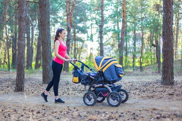 Naturspaziergang mit Kinderwagen, junge aktive Mutter in Sportkleidung spaziert mit ihrem Baby im Kinderwagen über den Waldweg und genießt die frische Luft — Stockfoto