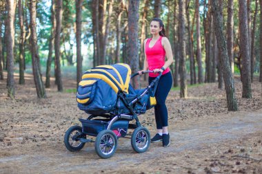 Bebek arabasıyla doğa yürüyüşü, spor giyimli genç aktif bir anne bebek arabasında bebeğiyle ormanda yürüyor, temiz havanın tadını çıkarıyor.