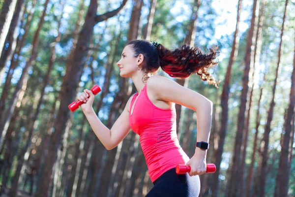 Side view of sportive attractive girl working out with dumbbells, training in the forest. Fitness, sport, lifestyle concept — Stock Photo, Image