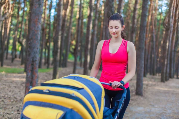 Nature walk with stroller, young active mother in sportswear walking on the forest walkway with her baby in the pram, enjoying fresh air — Stock Photo, Image