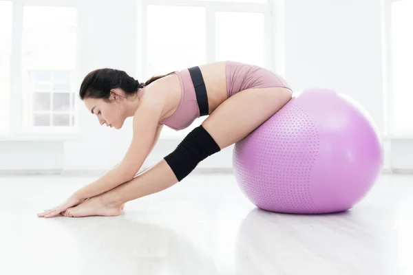 Slank sportief meisje doet stretching oefening reiken naar haar tenen zitten op fitness bal — Stockfoto