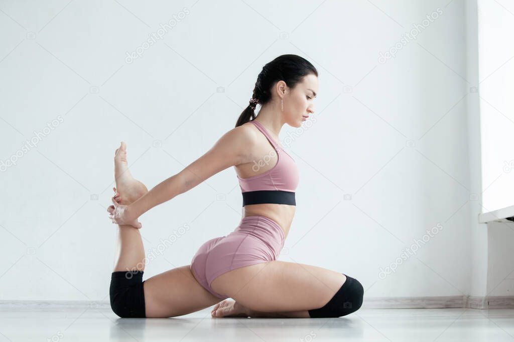 Young sporty woman in modern pink sportswear is sitting on the floor with bent leg doing stretching exercise