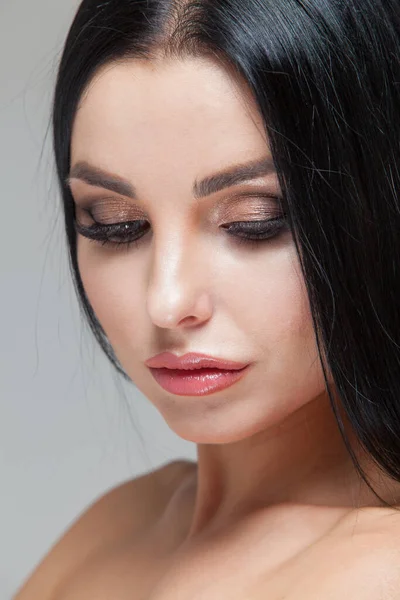 Närbild av vacker kvinna ansikte med skönhet makeup och lång brunett hår isolerad på grå bakgrund — Stockfoto