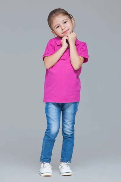 Full length portrait of funny active little girl wearing casual clothes: jeans and pink t-shirt isolated on grey studio background — 스톡 사진