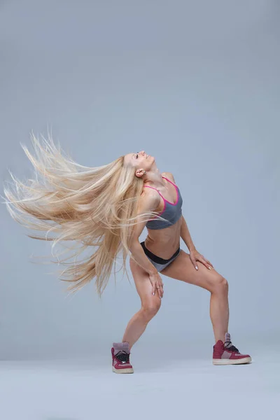 Сексуальна спортивна блондинка кинула довге волосся ізольовано на сірому фоні — стокове фото