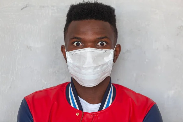 Tıbbi maske takan yakışıklı Afrikalı adamın yakın plan fotoğrafı gri arka planda Coronavirus 2019 tehlikesiyle şok oldu. Korku dolu gözler. — Stok fotoğraf